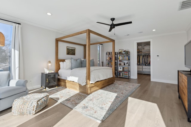 bedroom featuring a walk in closet, hardwood / wood-style flooring, ceiling fan, ornamental molding, and a closet