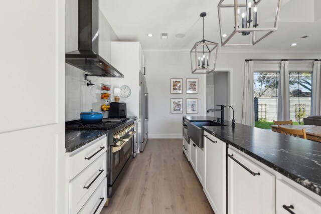 kitchen featuring wall chimney range hood, range with two ovens, white cabinets, a chandelier, and hanging light fixtures