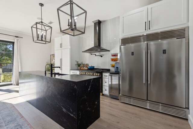 kitchen with premium appliances, wall chimney range hood, pendant lighting, light hardwood / wood-style flooring, and white cabinetry