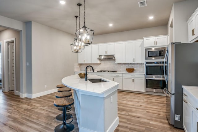 kitchen with visible vents, under cabinet range hood, a sink, backsplash, and appliances with stainless steel finishes