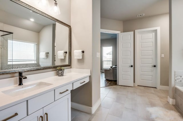 full bathroom with vanity, baseboards, visible vents, and tiled bath