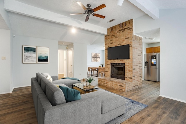 living room featuring ceiling fan, dark wood-type flooring, vaulted ceiling with beams, a textured ceiling, and a fireplace