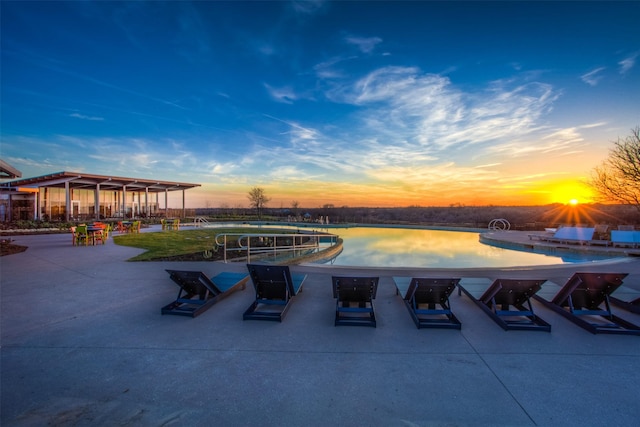 pool at dusk featuring a patio and a water view