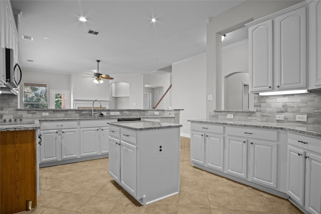 kitchen featuring light stone counters, a center island, decorative backsplash, white cabinetry, and ceiling fan