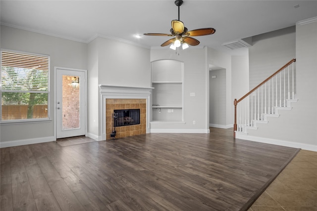 unfurnished living room with a tiled fireplace, built in features, ceiling fan, and crown molding