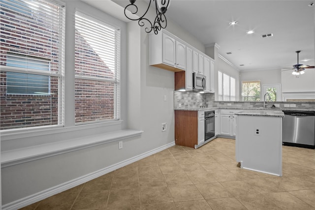 kitchen with light stone counters, stainless steel appliances, decorative backsplash, a kitchen island, and white cabinetry