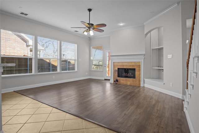 unfurnished living room with a tile fireplace, crown molding, light tile patterned floors, ceiling fan, and built in shelves