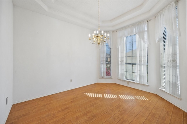 spare room featuring a raised ceiling, basketball hoop, a chandelier, and wood-type flooring