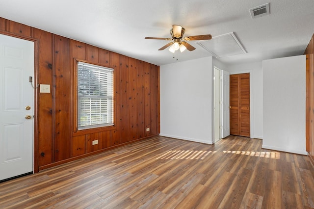 interior space with a textured ceiling, ceiling fan, wood walls, and dark wood-type flooring