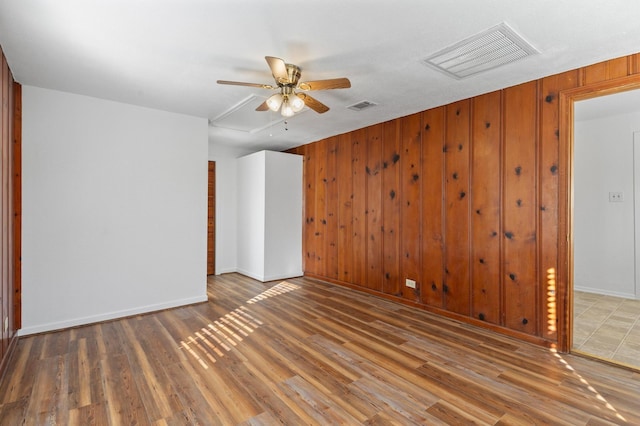 empty room with wooden walls, ceiling fan, and wood-type flooring