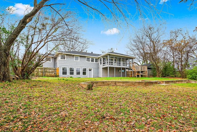 rear view of house featuring a wooden deck, a lawn, and a sunroom