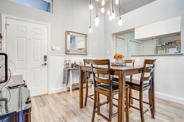 dining area featuring light wood-type flooring and a towering ceiling