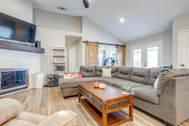 living room featuring french doors, light wood-type flooring, ceiling fan, a barn door, and high vaulted ceiling