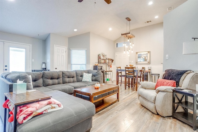 living room featuring ceiling fan with notable chandelier, a healthy amount of sunlight, vaulted ceiling, and light hardwood / wood-style flooring