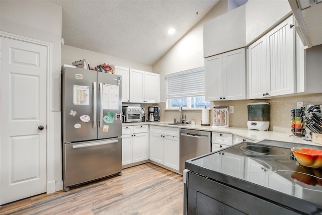 kitchen featuring white cabinetry, sink, stainless steel appliances, vaulted ceiling, and decorative backsplash