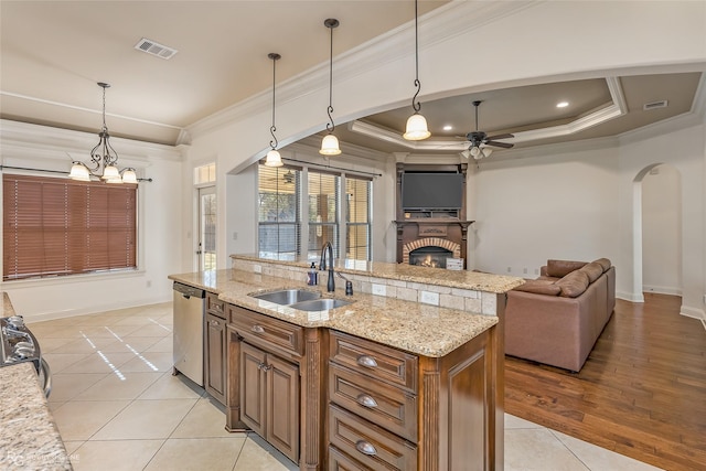 kitchen featuring sink, a kitchen island with sink, hanging light fixtures, light stone counters, and stainless steel dishwasher