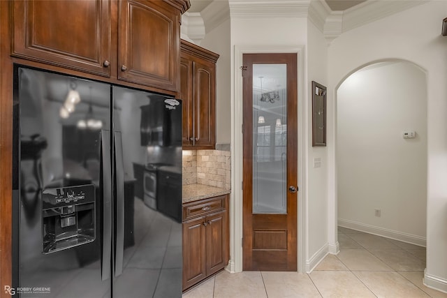 kitchen featuring light tile patterned flooring, black fridge, light stone counters, ornamental molding, and decorative backsplash