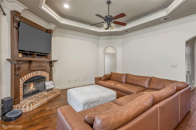 living room featuring crown molding, dark hardwood / wood-style floors, a tray ceiling, ceiling fan, and a fireplace