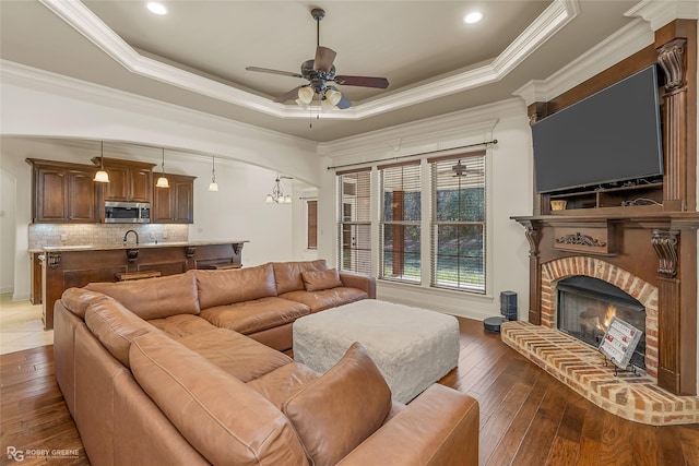 living room featuring ornamental molding, dark hardwood / wood-style floors, a tray ceiling, ceiling fan, and a fireplace