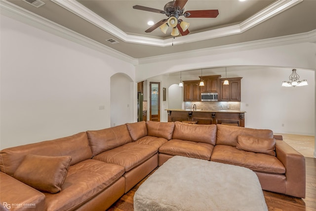 living room with a raised ceiling, ornamental molding, hardwood / wood-style floors, and ceiling fan with notable chandelier