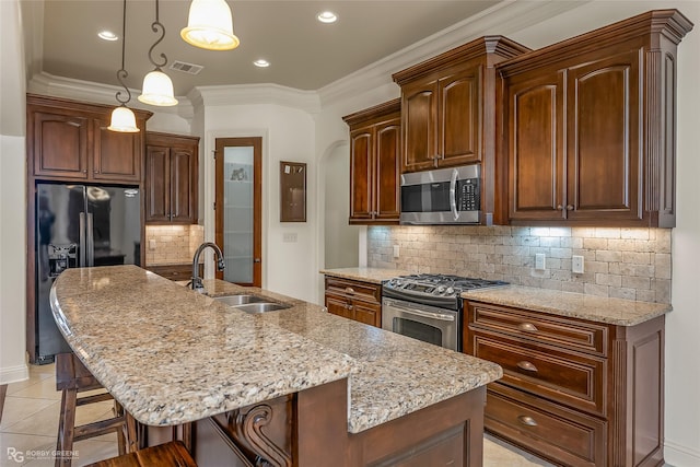 kitchen with appliances with stainless steel finishes, a kitchen island with sink, sink, and decorative light fixtures