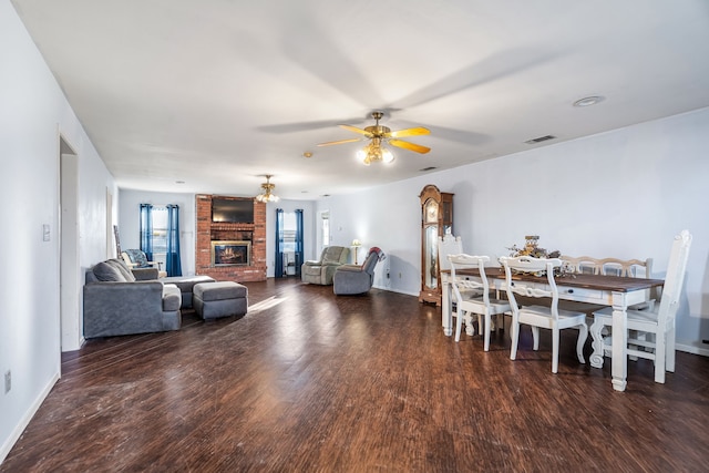 dining room featuring ceiling fan, dark wood-type flooring, and a brick fireplace