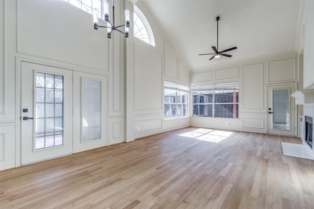 unfurnished living room with ceiling fan with notable chandelier, light hardwood / wood-style floors, high vaulted ceiling, and ornamental molding