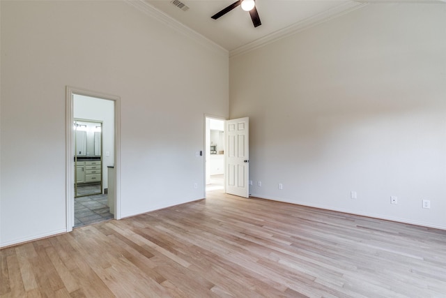 spare room featuring light wood-type flooring, ceiling fan, a high ceiling, and ornamental molding