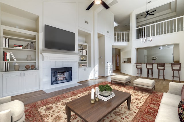 living room featuring a tile fireplace, a high ceiling, built in shelves, ceiling fan, and dark hardwood / wood-style floors