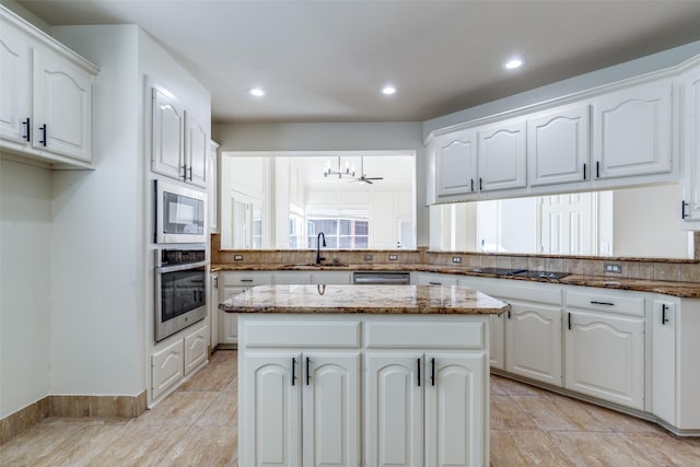 kitchen featuring a kitchen island, appliances with stainless steel finishes, stone countertops, white cabinetry, and sink