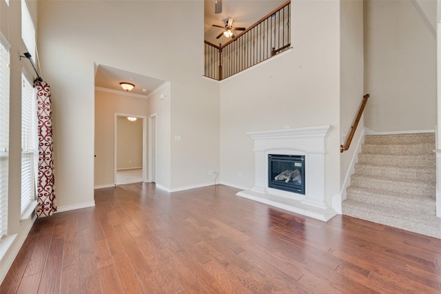 unfurnished living room featuring a high ceiling, ornamental molding, hardwood / wood-style floors, and ceiling fan