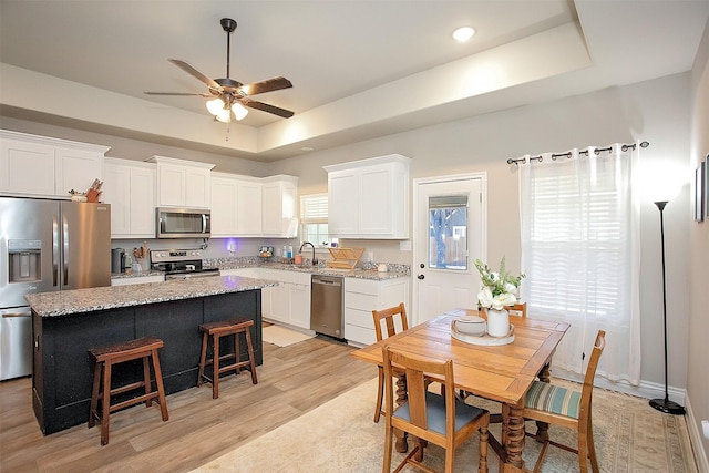 kitchen with a kitchen island, light stone counters, appliances with stainless steel finishes, and a tray ceiling