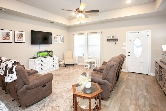 living room with light wood-type flooring, a tray ceiling, and ceiling fan