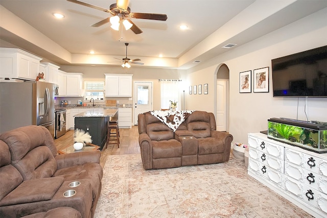 living room with a tray ceiling, ceiling fan, light hardwood / wood-style floors, and sink