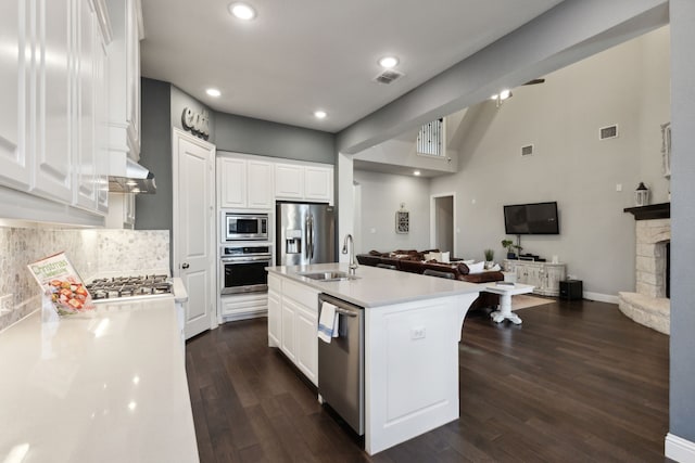 kitchen featuring stainless steel appliances, white cabinets, open floor plan, light countertops, and a center island with sink