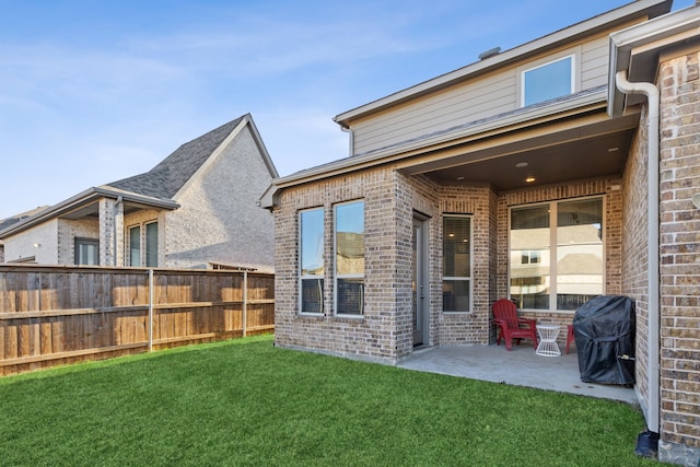 back of house with a patio area, a yard, fence, and brick siding