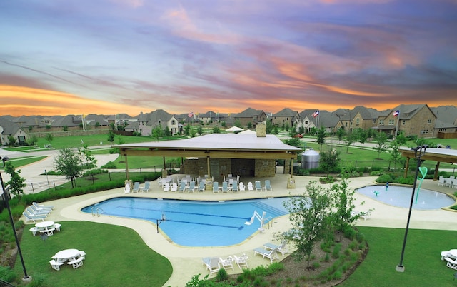 pool at dusk with a community pool, fence, a patio, and a residential view