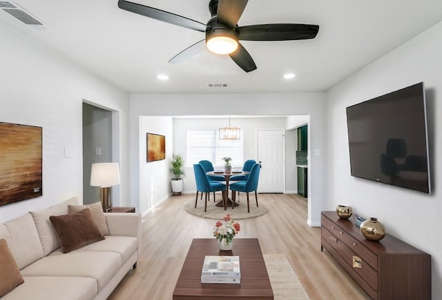 living room with ceiling fan with notable chandelier and light hardwood / wood-style flooring