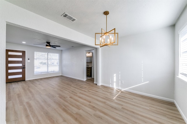 unfurnished living room with ceiling fan with notable chandelier, a textured ceiling, and light hardwood / wood-style flooring