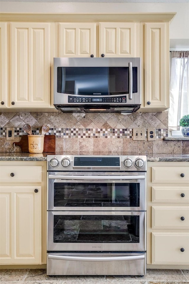 kitchen with decorative backsplash, light stone counters, stainless steel appliances, and cream cabinets