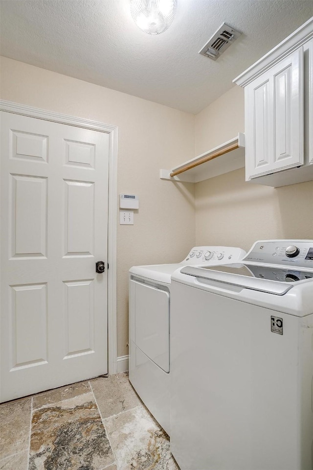 washroom with cabinets, a textured ceiling, and washer and clothes dryer