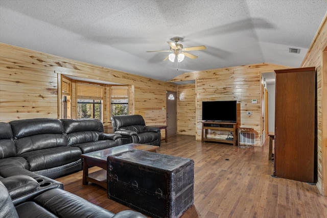 living room featuring wooden walls, a ceiling fan, visible vents, lofted ceiling, and hardwood / wood-style flooring