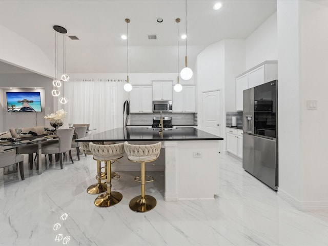 kitchen featuring decorative light fixtures, white cabinetry, backsplash, a kitchen island with sink, and stainless steel appliances