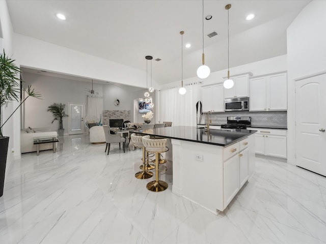 kitchen with appliances with stainless steel finishes, white cabinetry, tasteful backsplash, a center island with sink, and decorative light fixtures