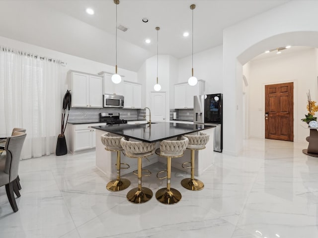 kitchen with appliances with stainless steel finishes, an island with sink, sink, white cabinets, and hanging light fixtures