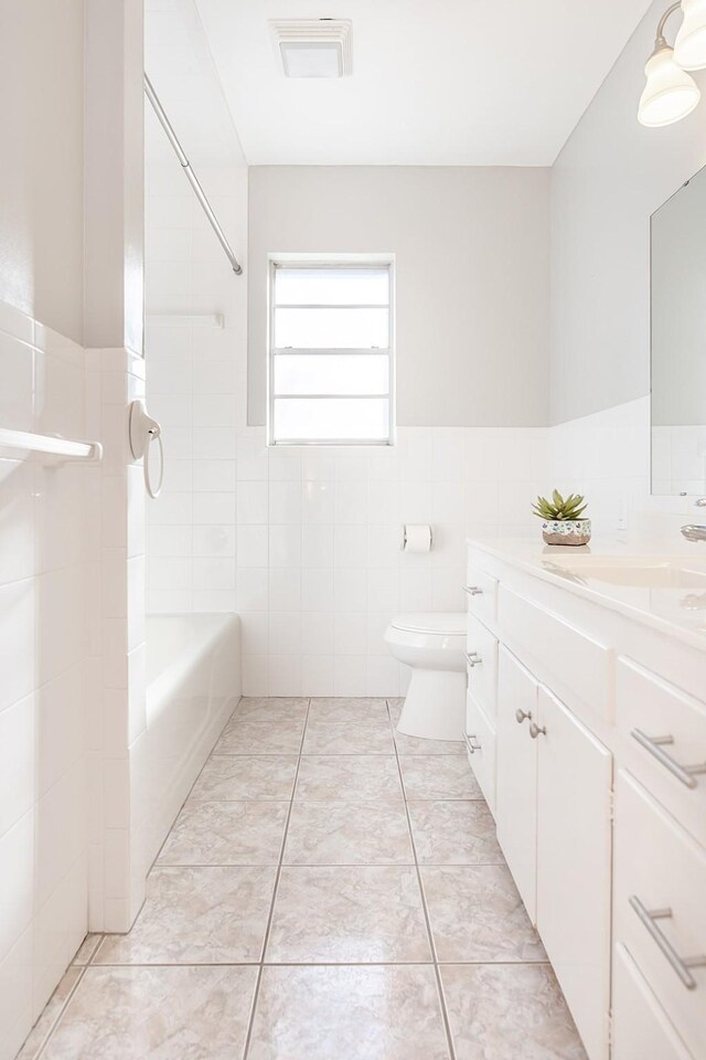 full bathroom featuring vanity, tile patterned floors, tiled shower / bath combo, toilet, and tile walls