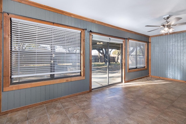 interior space with ceiling fan, ornamental molding, and wooden walls