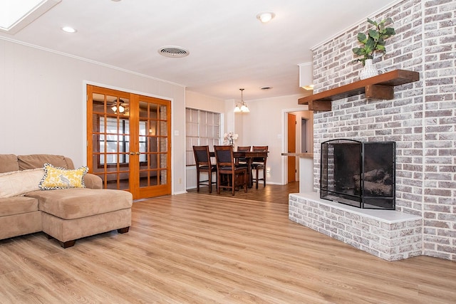 living room with crown molding, a fireplace, light hardwood / wood-style floors, and french doors