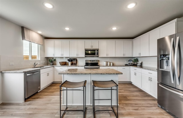 kitchen with sink, appliances with stainless steel finishes, light stone counters, white cabinets, and a kitchen island