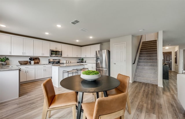 kitchen with appliances with stainless steel finishes, a kitchen island, white cabinetry, light hardwood / wood-style floors, and light stone countertops